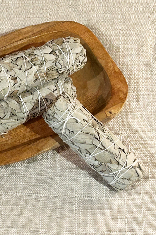 A Rabbit Rabbit Smudge Stick laying on a table cloth leaned against wooden bowl